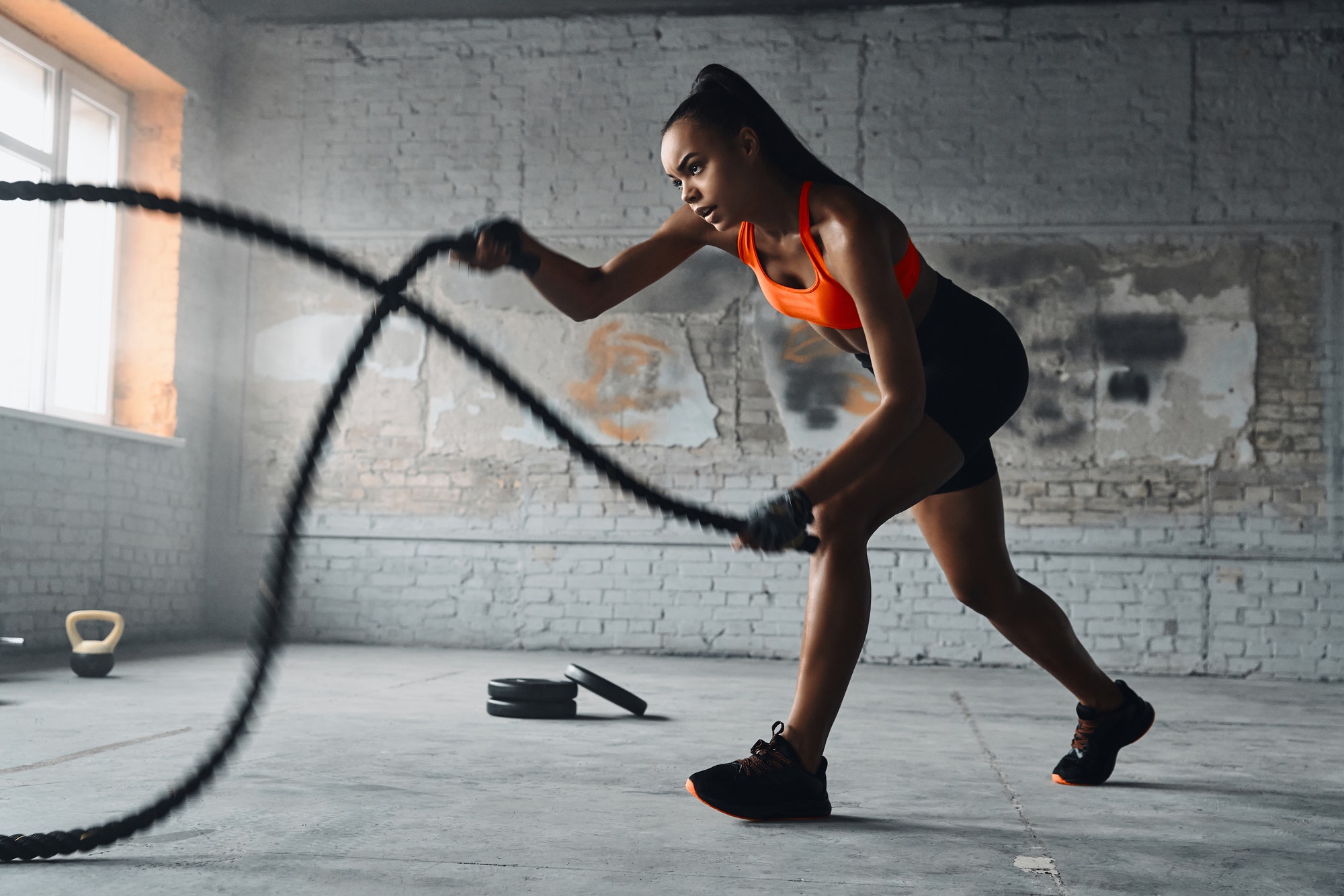 Concentrated young African woman exercising with battle ropes in gym